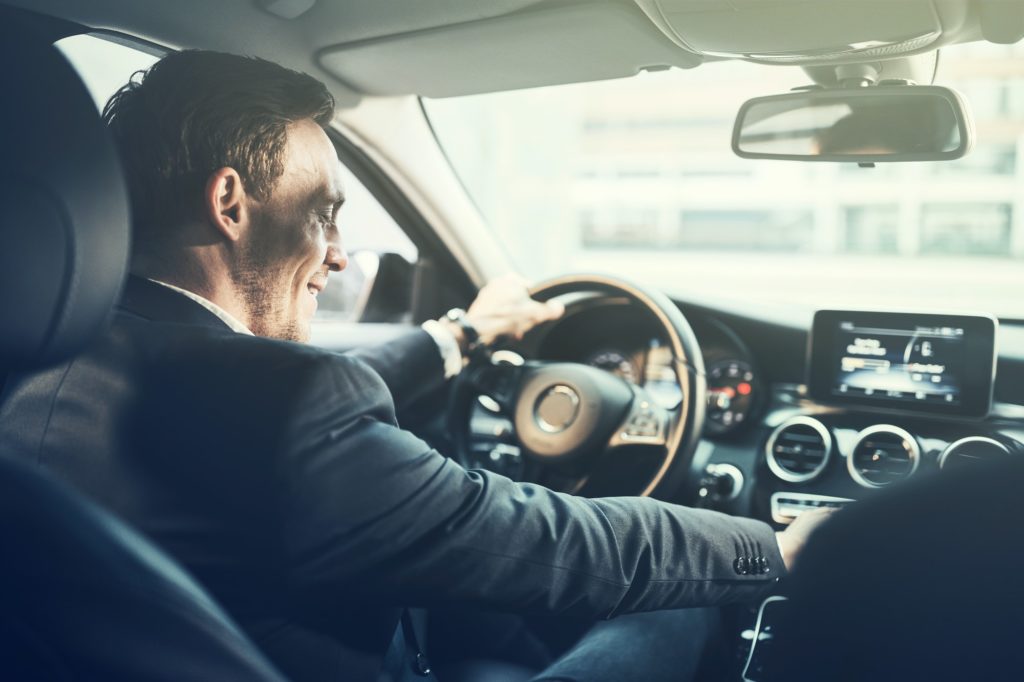 Smiling young businessman changing music stations while driving