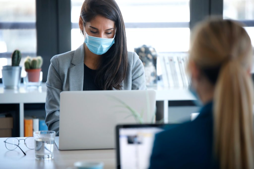 business women wearing a hygienic face mask while work with laptops in the coworking space.