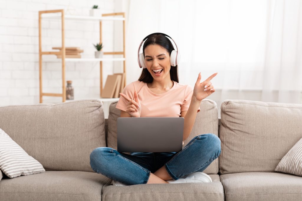 Woman listening to music in headphones on couch, using pc