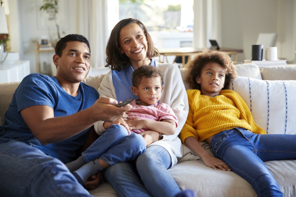 Front view of young family sitting together on the sofa in their living room watching TV