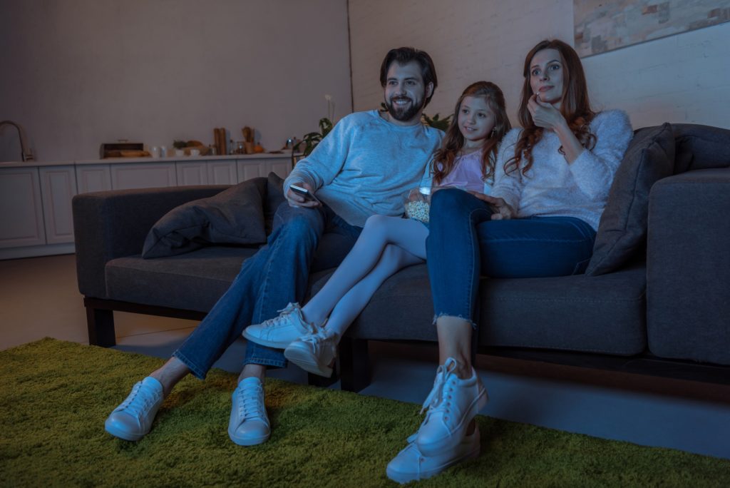 smiling parents and daughter watching tv with popcorn