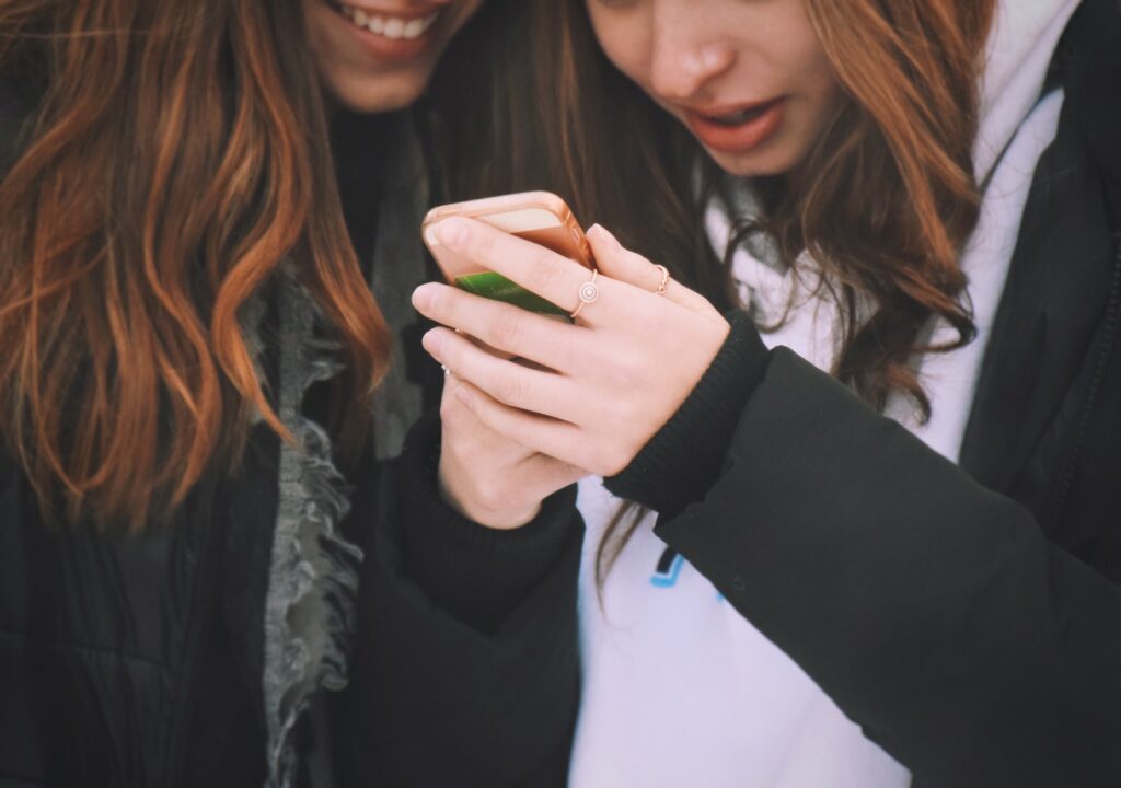 Two young teenage girls friends looking at something on a mobile phone and smiling