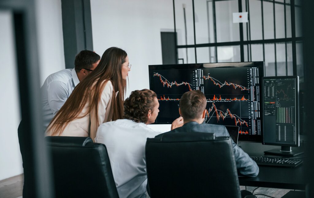 Tracks the graphs. Team of stockbrokers works in modern office with many display screens