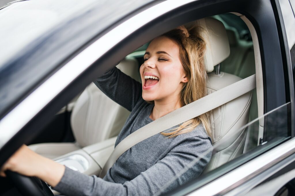 Cheerful young woman driver sitting in car, driving.