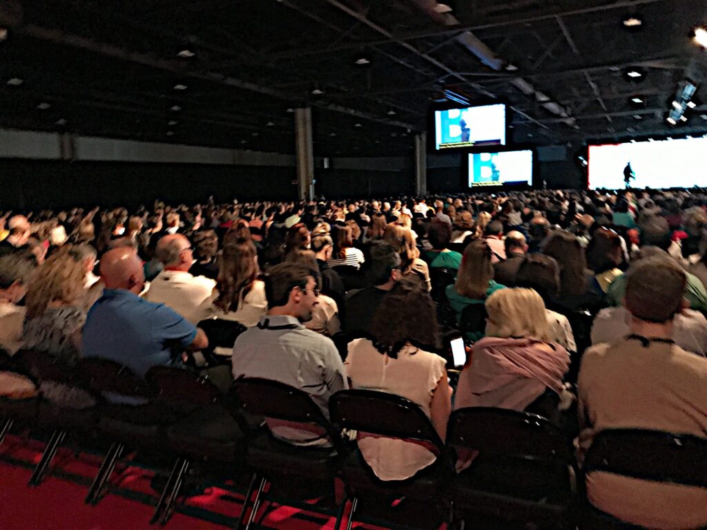 Large Audience crowd gathering at a conference watching the guest speaker on the main stage