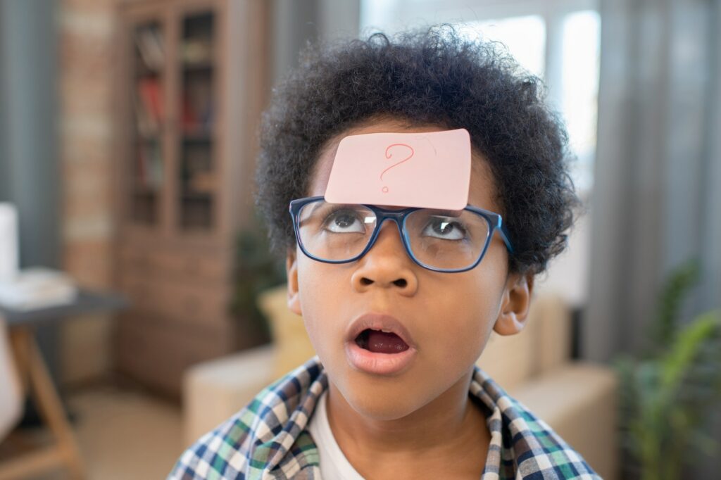 Cute and funny boy looking at notepaper with question mark on his forehead