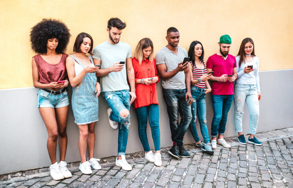 Multicultural milenials using smartphone against wall at university college backyard