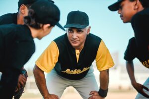 Keep doing what you are doing. Shot of a baseball coach talking to his team while out on the pitch.